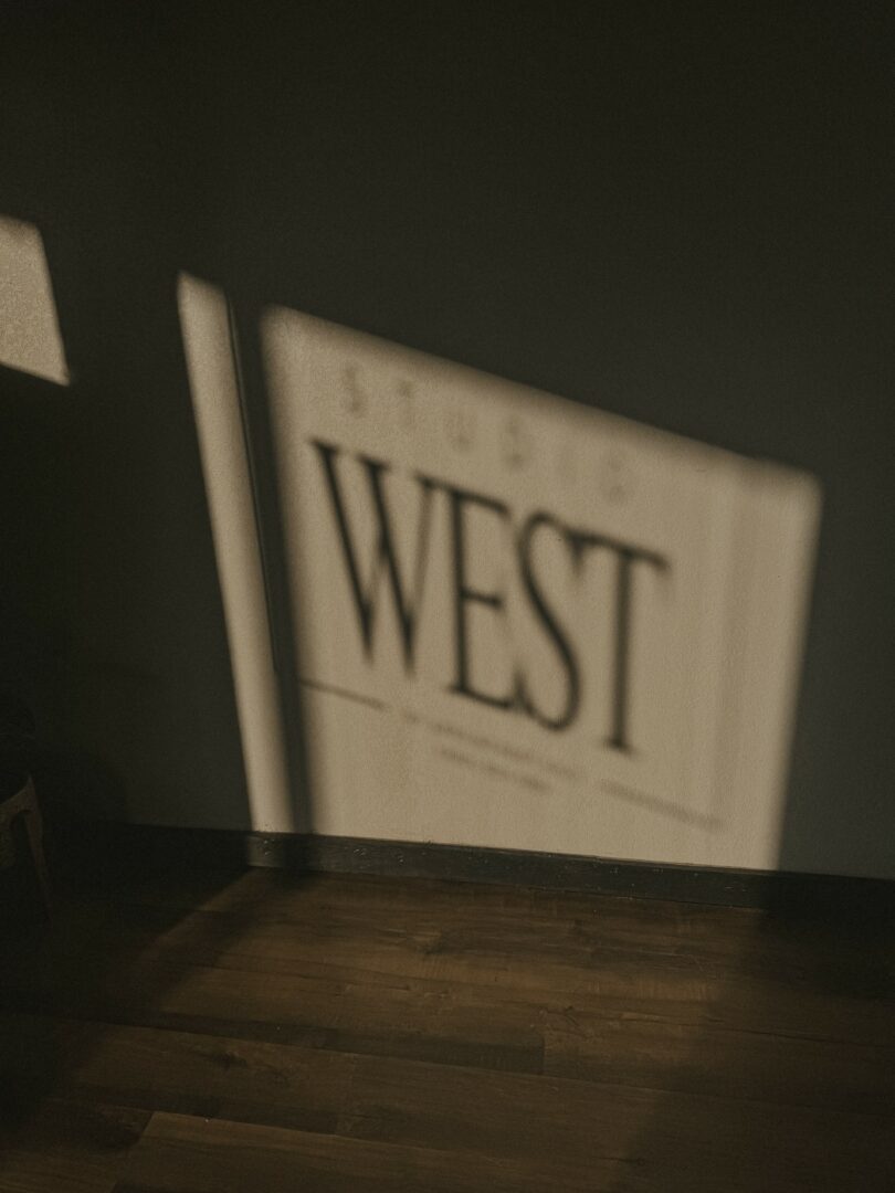 Blurred sign with the word 'WEST' on a wall, with shadow and light patterns.