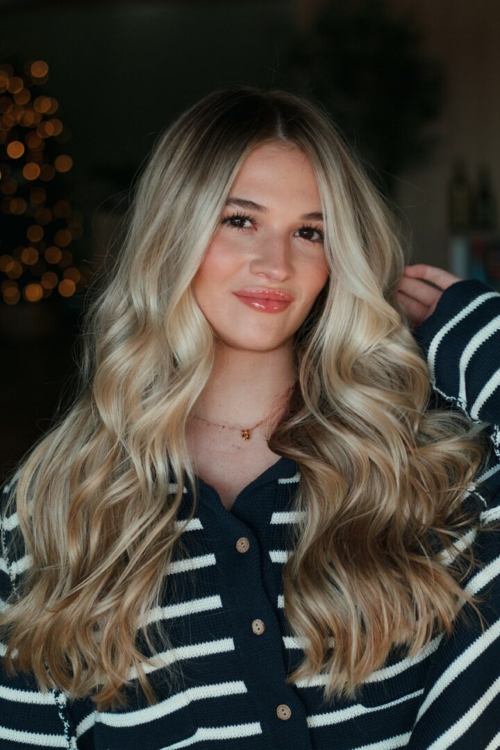 Young woman with long, wavy blonde hair and a striped navy and white shirt, smiling softly.
