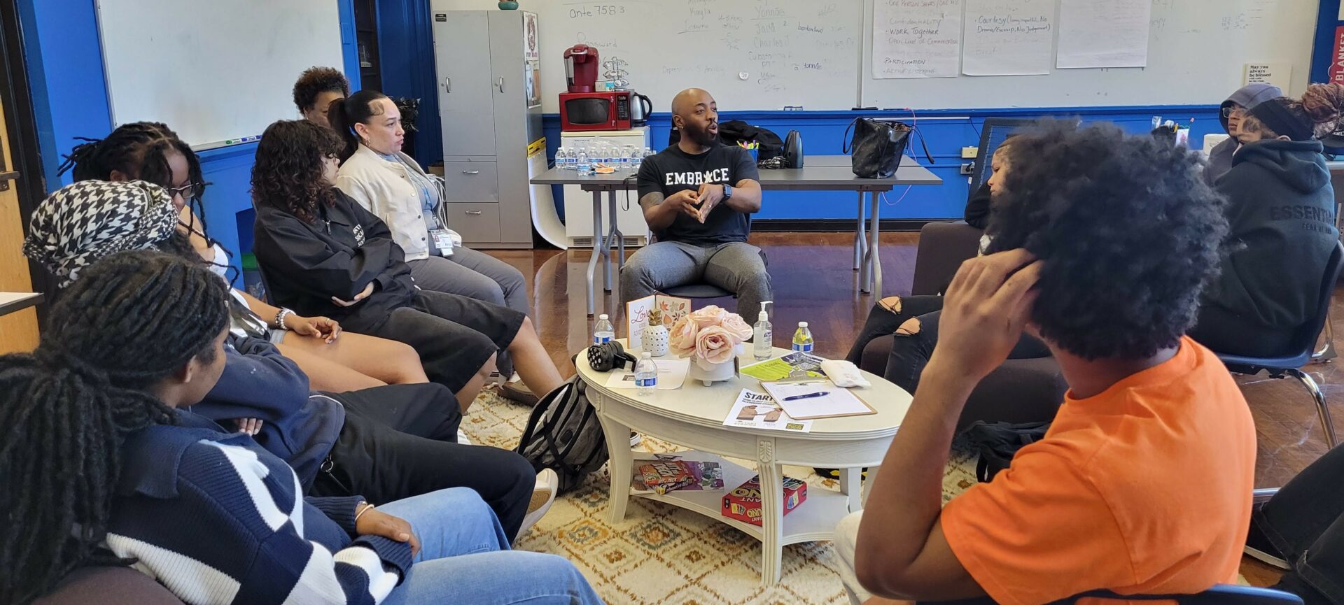 Group of people seated in a circle around a person speaking in a classroom setting.
