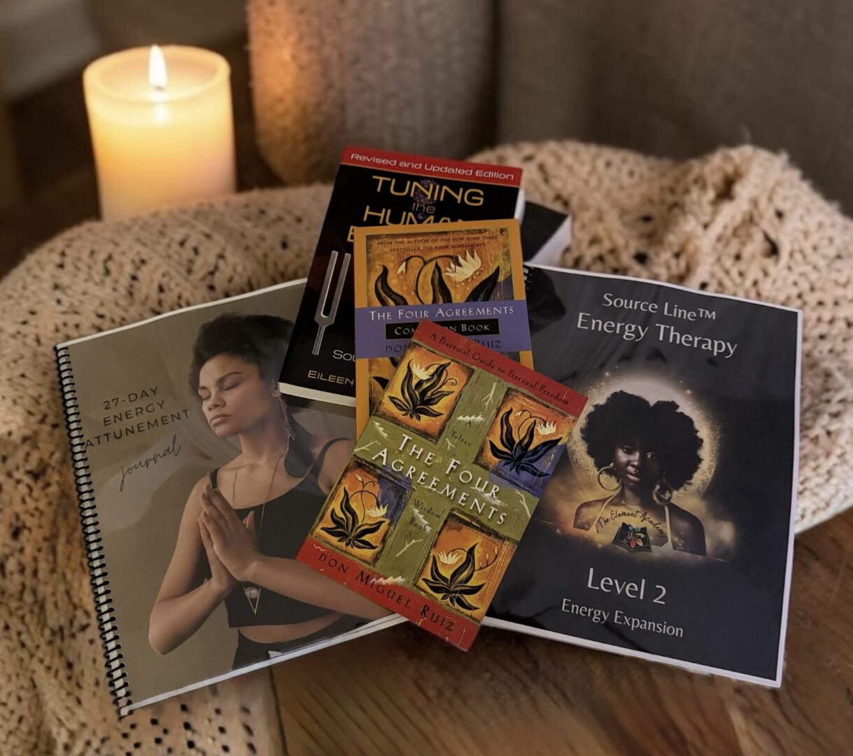 Collection of books and cards on a bed with a lit candle in the background.