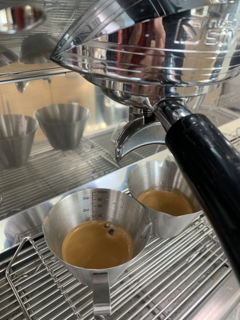 Espresso machine pouring coffee into two metal cups with dark liquid, on a metal drip tray.
