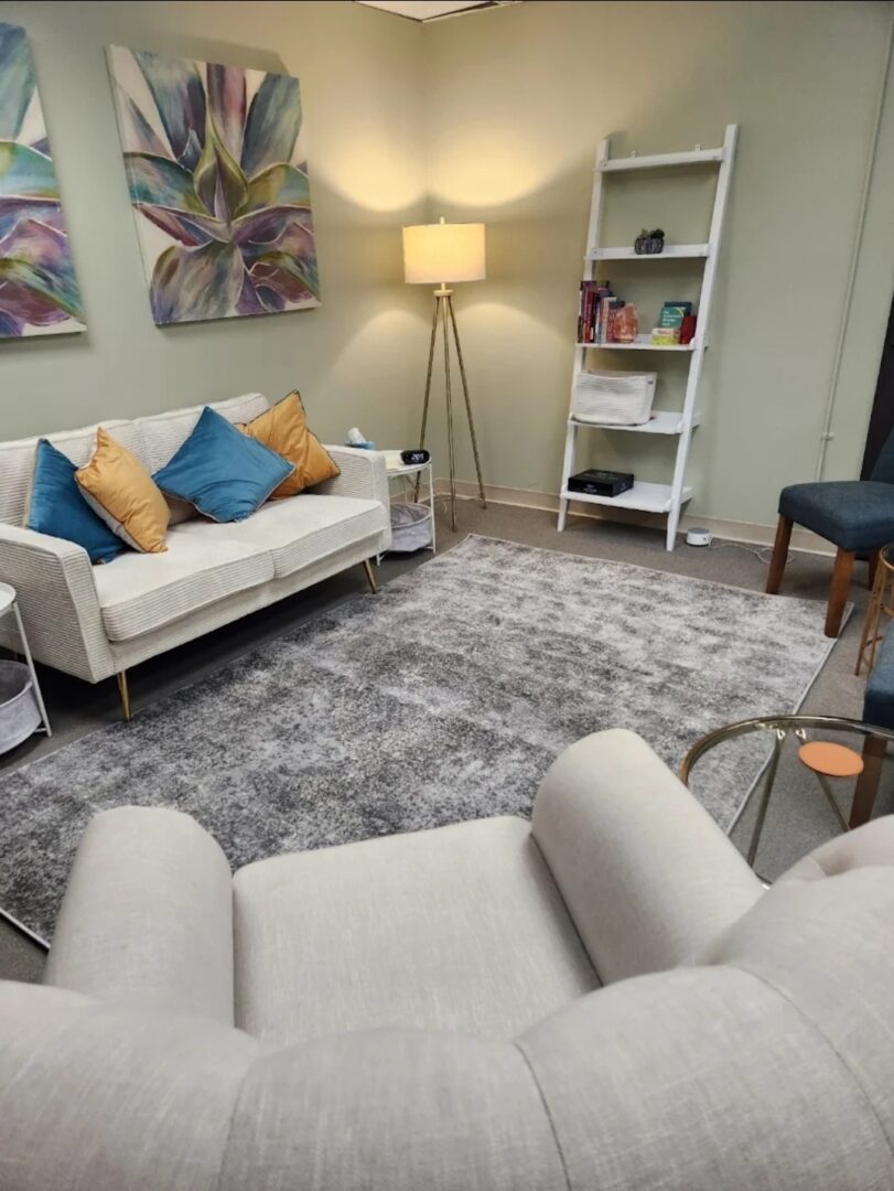Living room with white sofa, armchair, bookshelf, floor lamp, and colorful artwork on wall.