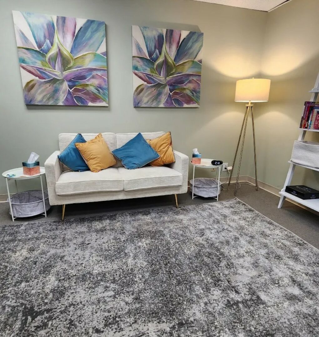 Living room with a white sofa, colorful pillows, two side tables, a floor lamp, and abstract wall art.