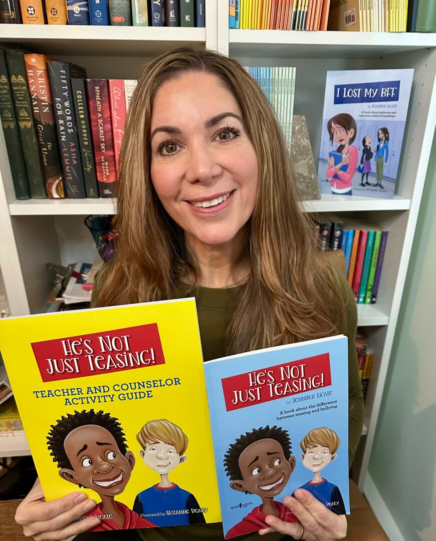 Woman smiling holding two books in front of bookshelves, one yellow and one blue, with illustrated children on covers.