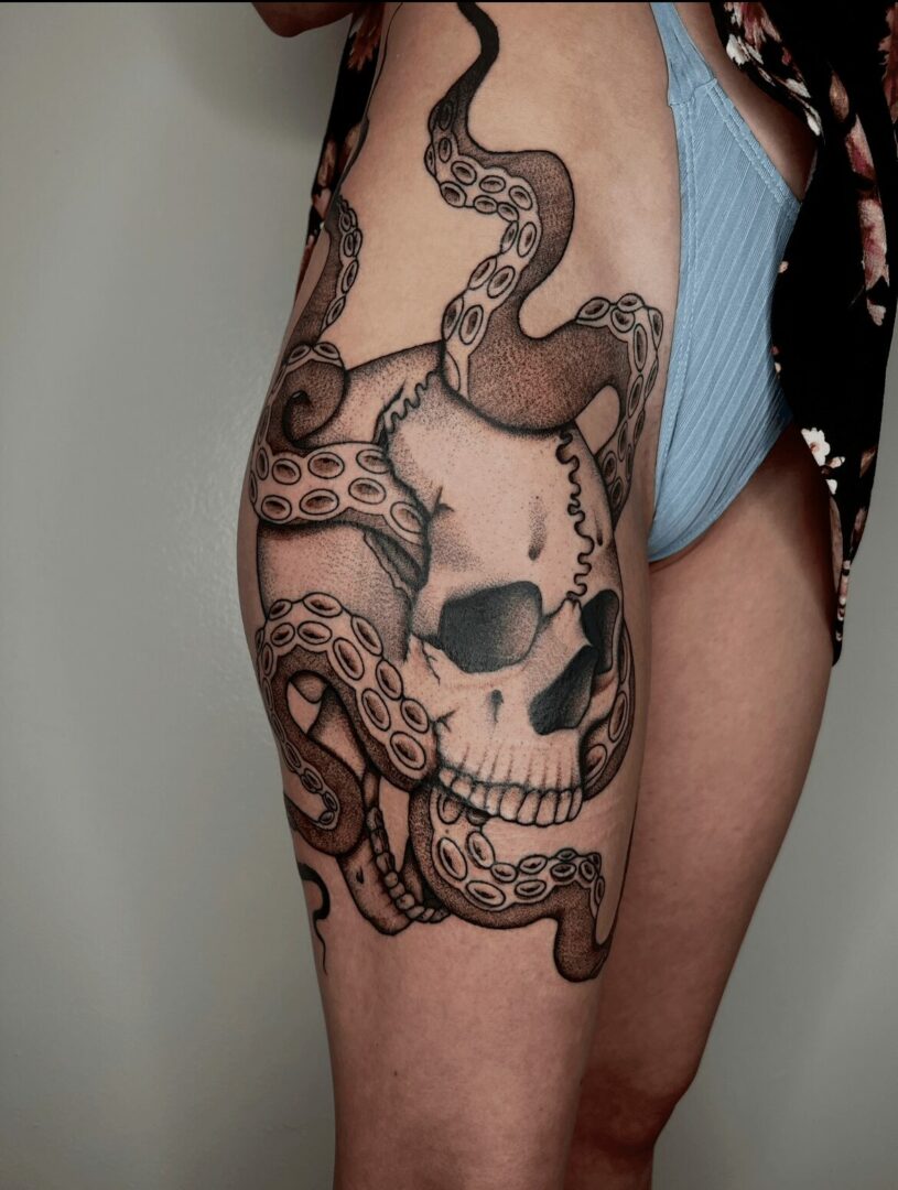 Tattoo of a skull with a snake and octopus tentacles on a person's thigh.