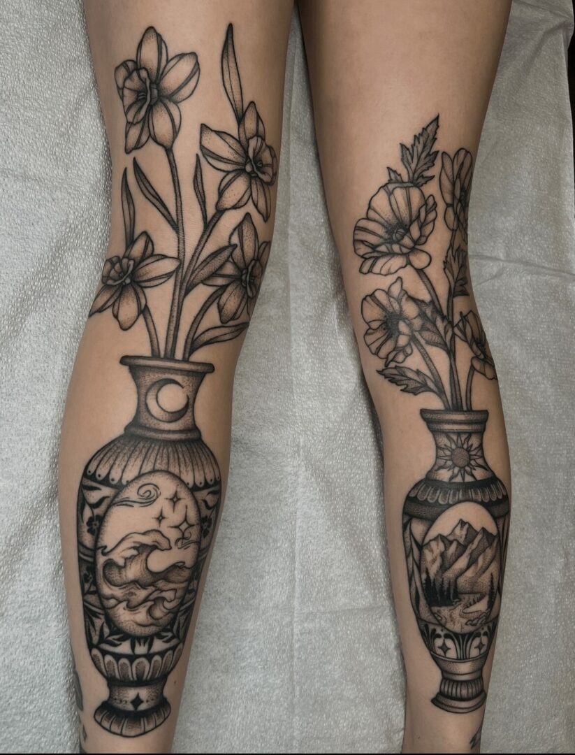 Two legs with black line floral and vase tattoos, detailed with flowers and landscape scenes.