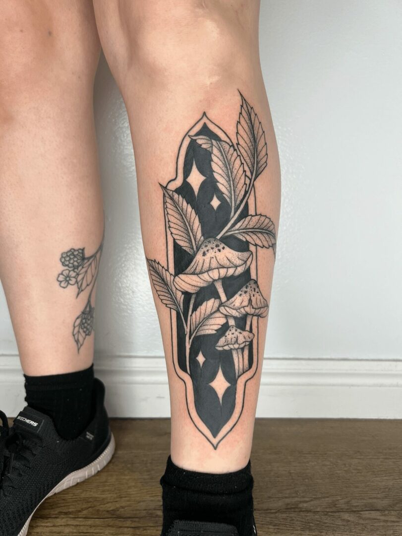 Black and gray tattoo of mushrooms and leaves on person's lower leg.