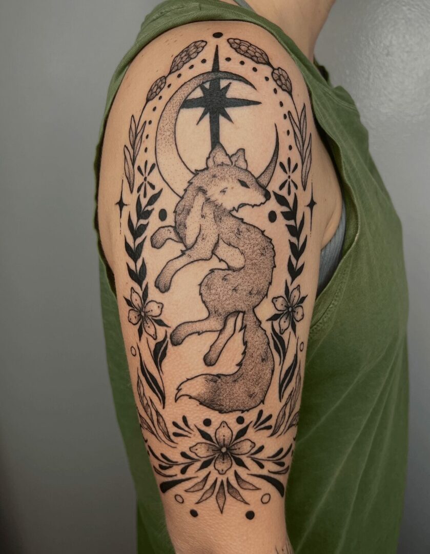Tattoo of a fox surrounded by floral and celestial designs on upper arm.